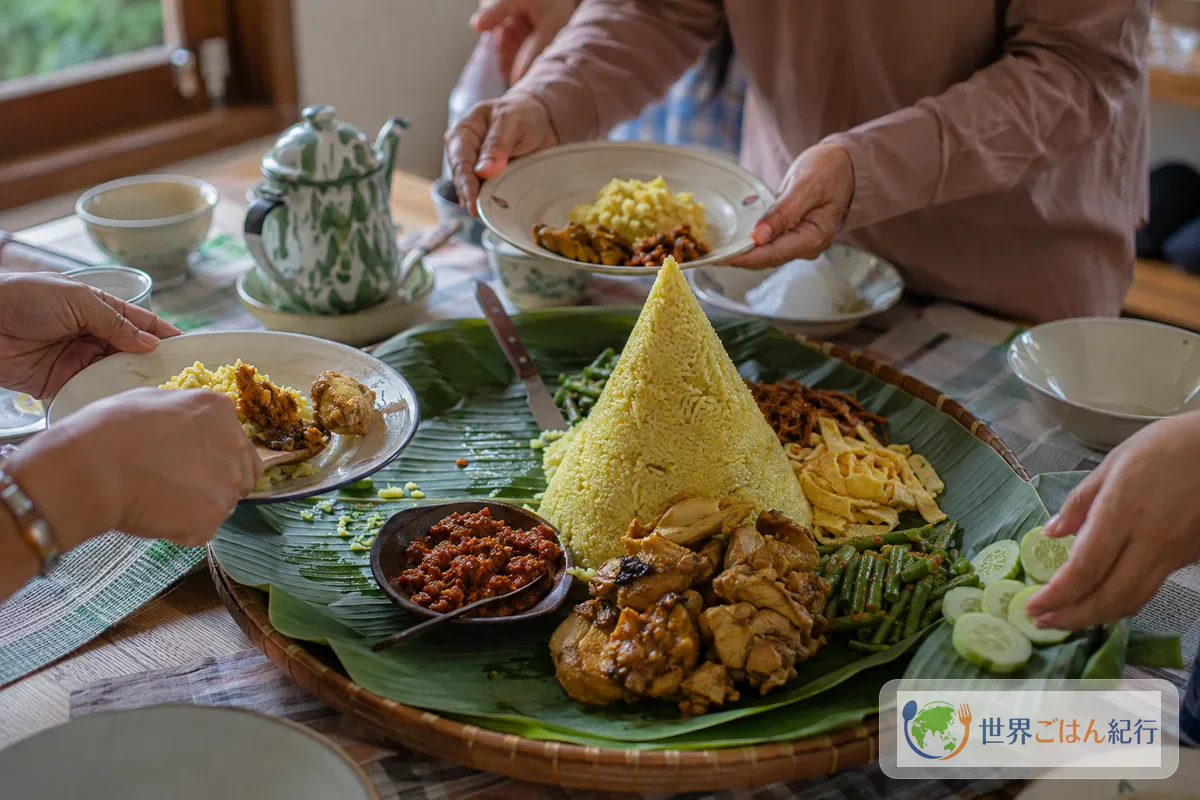バナナの葉を敷いた台のナシトゥンペンを家族の手で取り分ける食卓